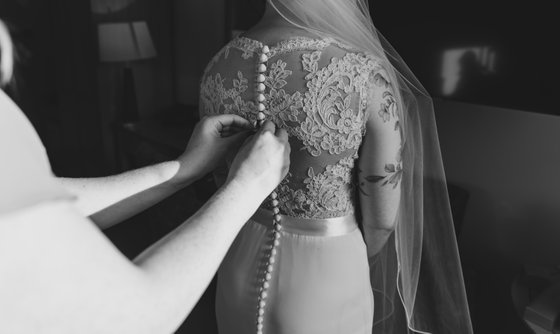 Bride having her wedding dress buttoned up at The Tithe Barn Bedford